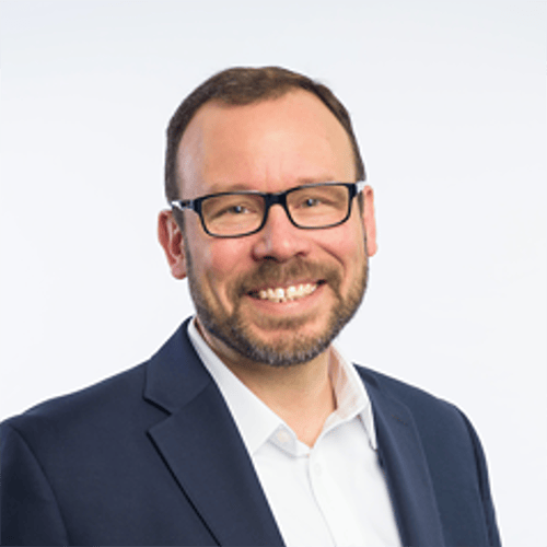 Smiling man with glasses and beard in a blue suit.