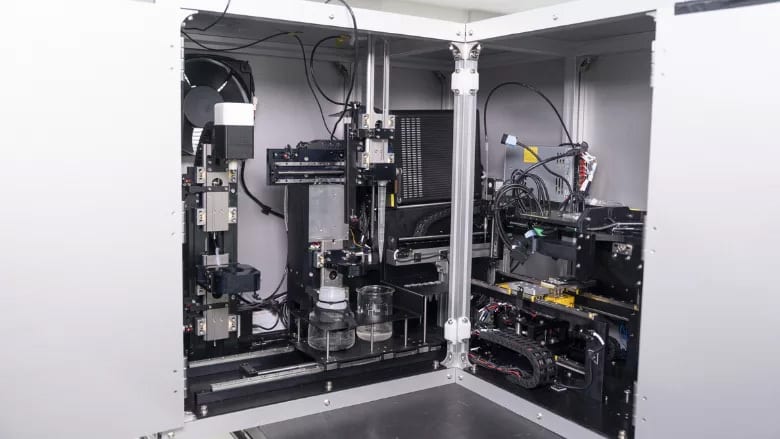 Interior of an automated laboratory liquid handling system with a robotic arm and beakers.