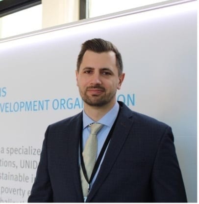 Man in a suit smiling in front of a banner for a development organization.