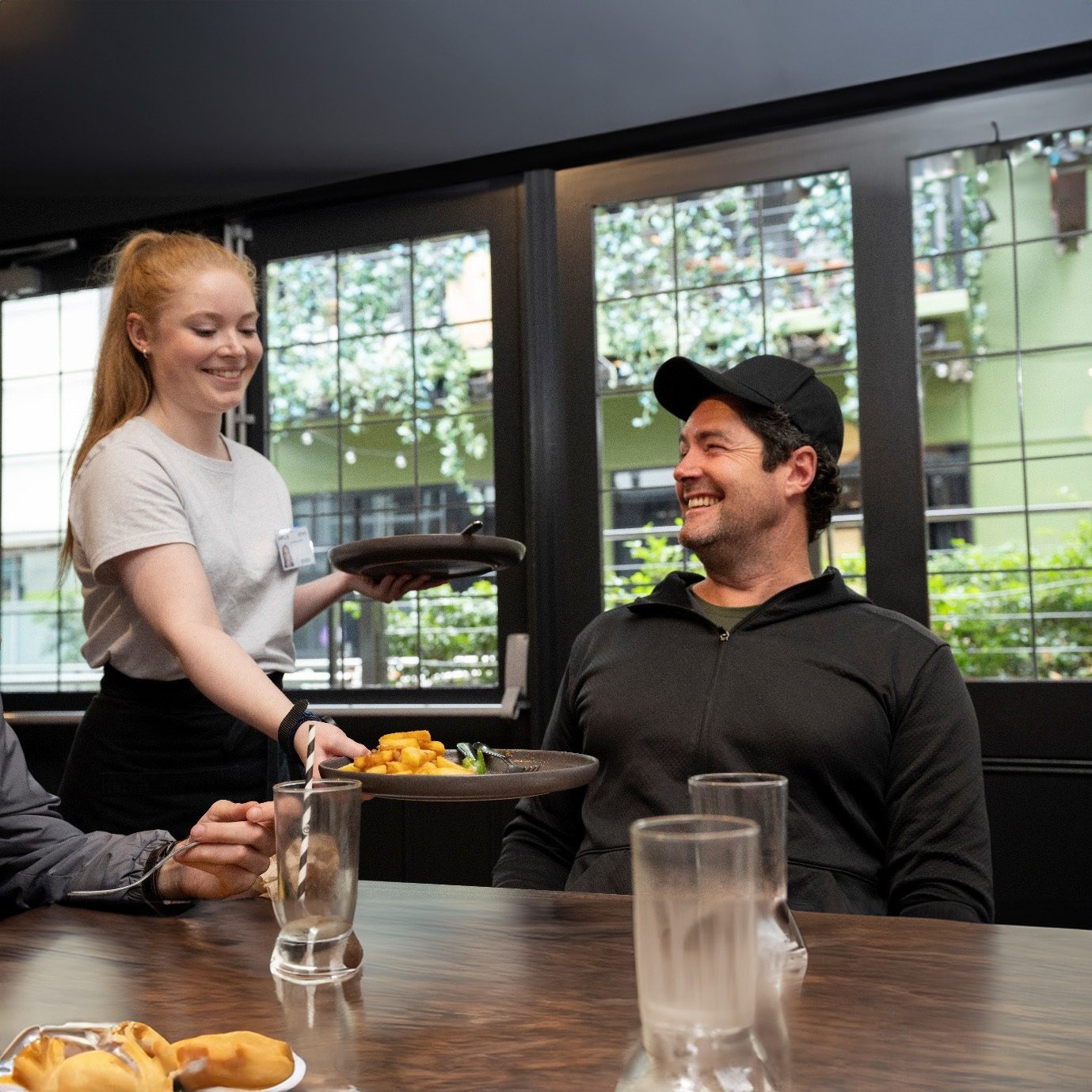 Waitress serves food to a smiling man in a restaurant, with another person at the table.