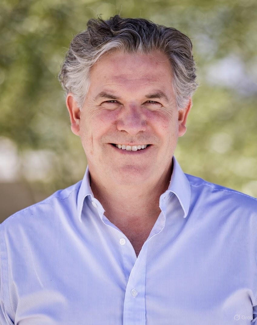Headshot of a smiling man with gray hair and a blue striped shirt.