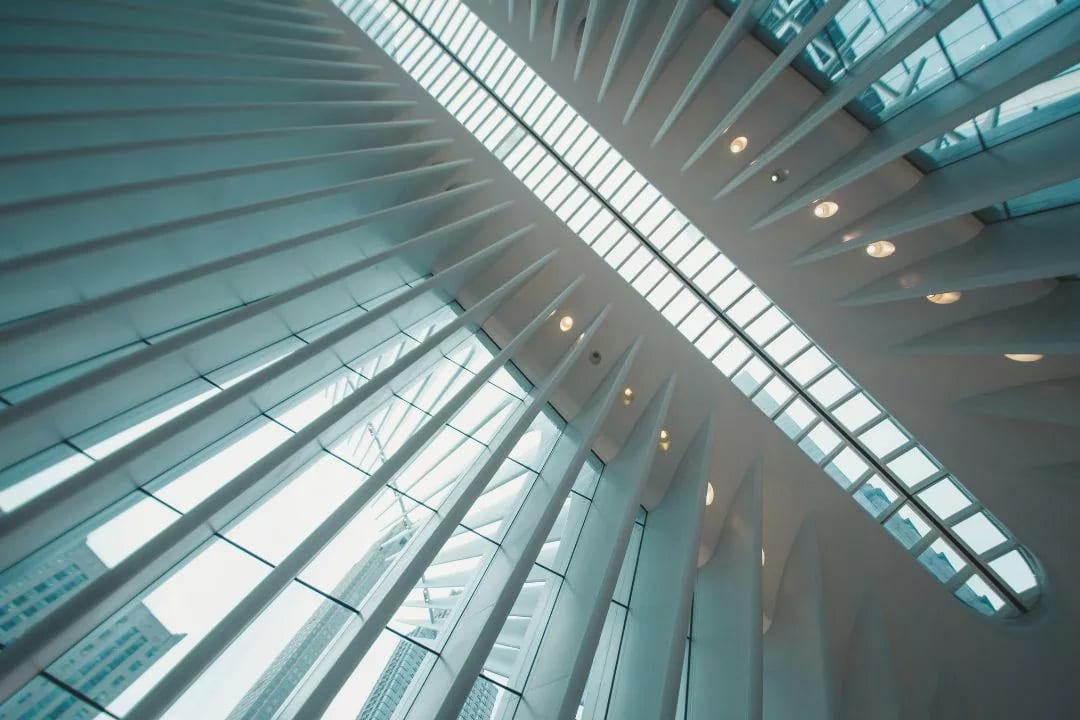 Architectural interior with white ribbed structures, a diagonal skylight, and reflections on glass.