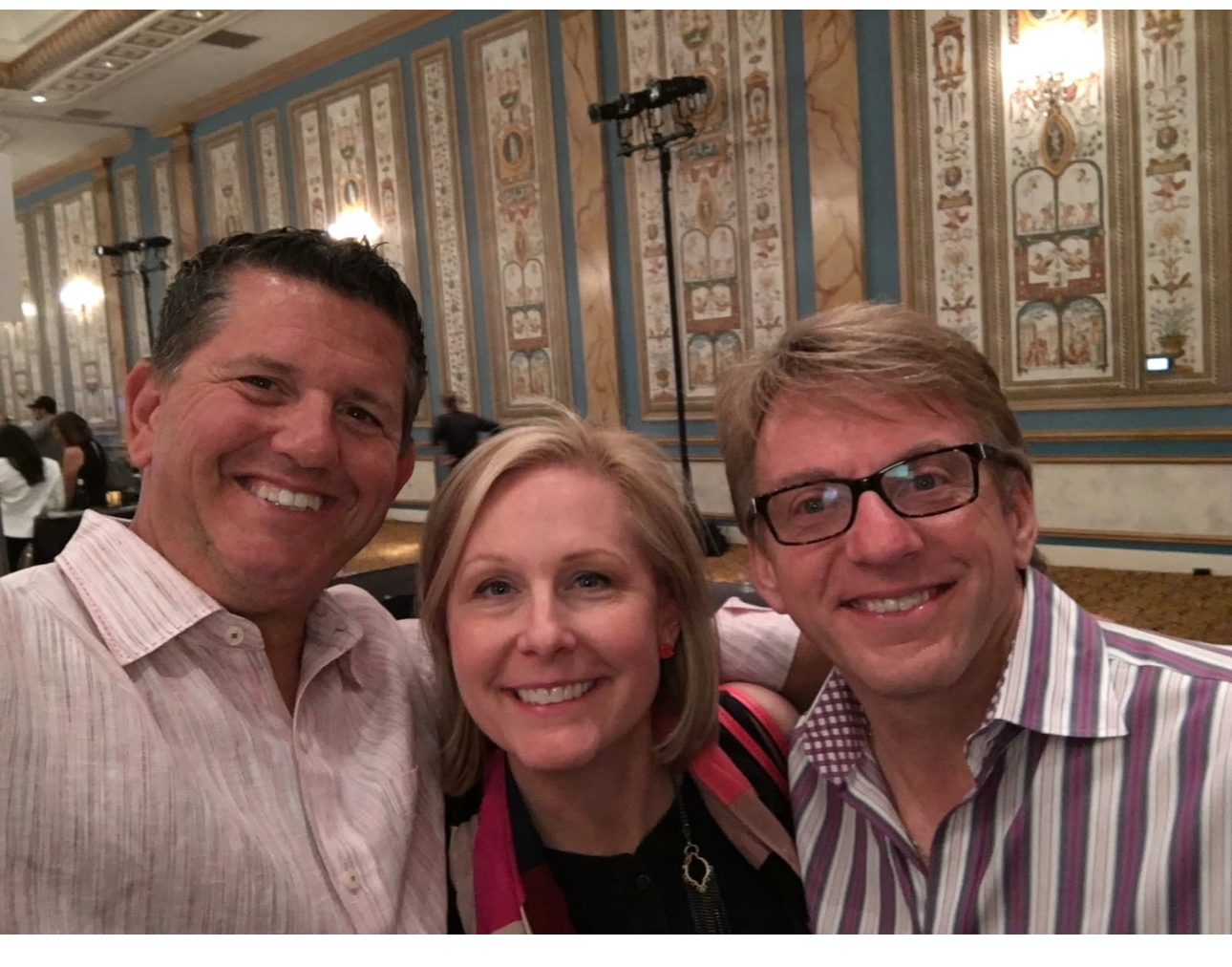 Smiling selfie of three adults (two men, one woman) indoors.