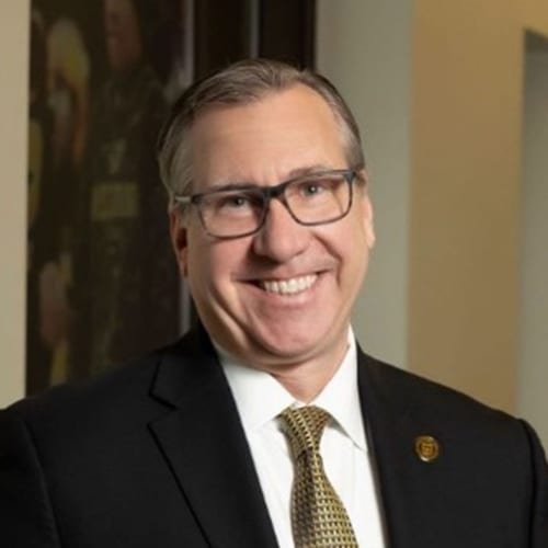 Smiling man in suit, tie, and glasses.