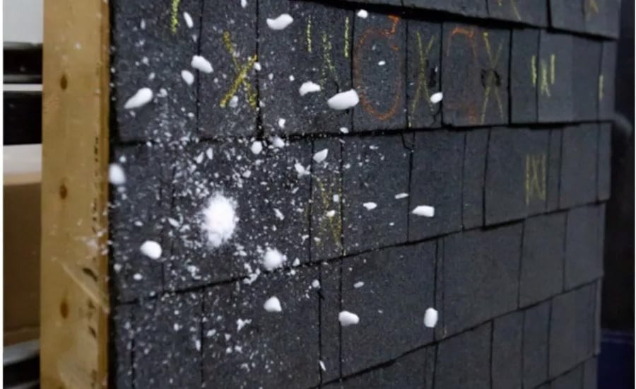 Dark shingle-like wall covered in white pellets, next to a wooden beam.
