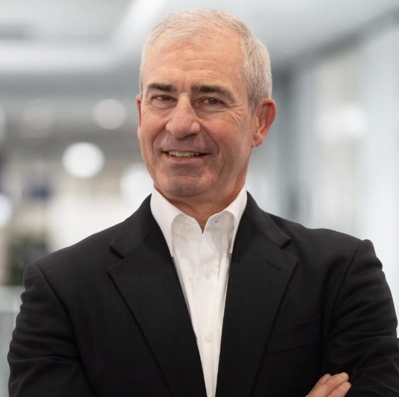 A smiling man in a suit with gray hair and crossed arms.