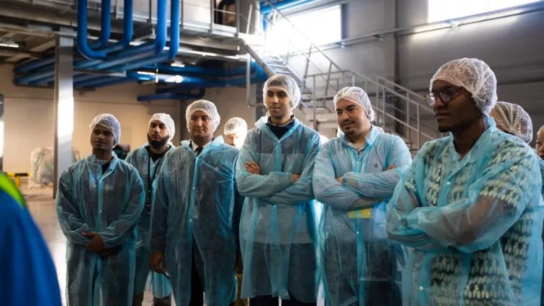 A group of men in hairnets and blue protective gowns on a tour inside an industrial facility.