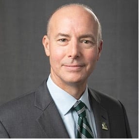 Smiling bald man in a suit and green striped tie.