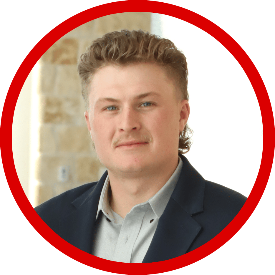 Headshot of a young man with a light mustache, blue eyes, wearing a suit jacket in a red circular frame.