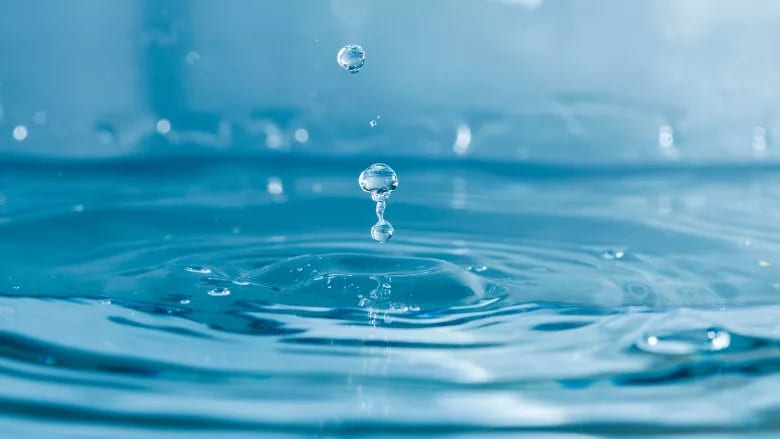 Two water droplets falling into a blue water surface, creating ripples and splashes.