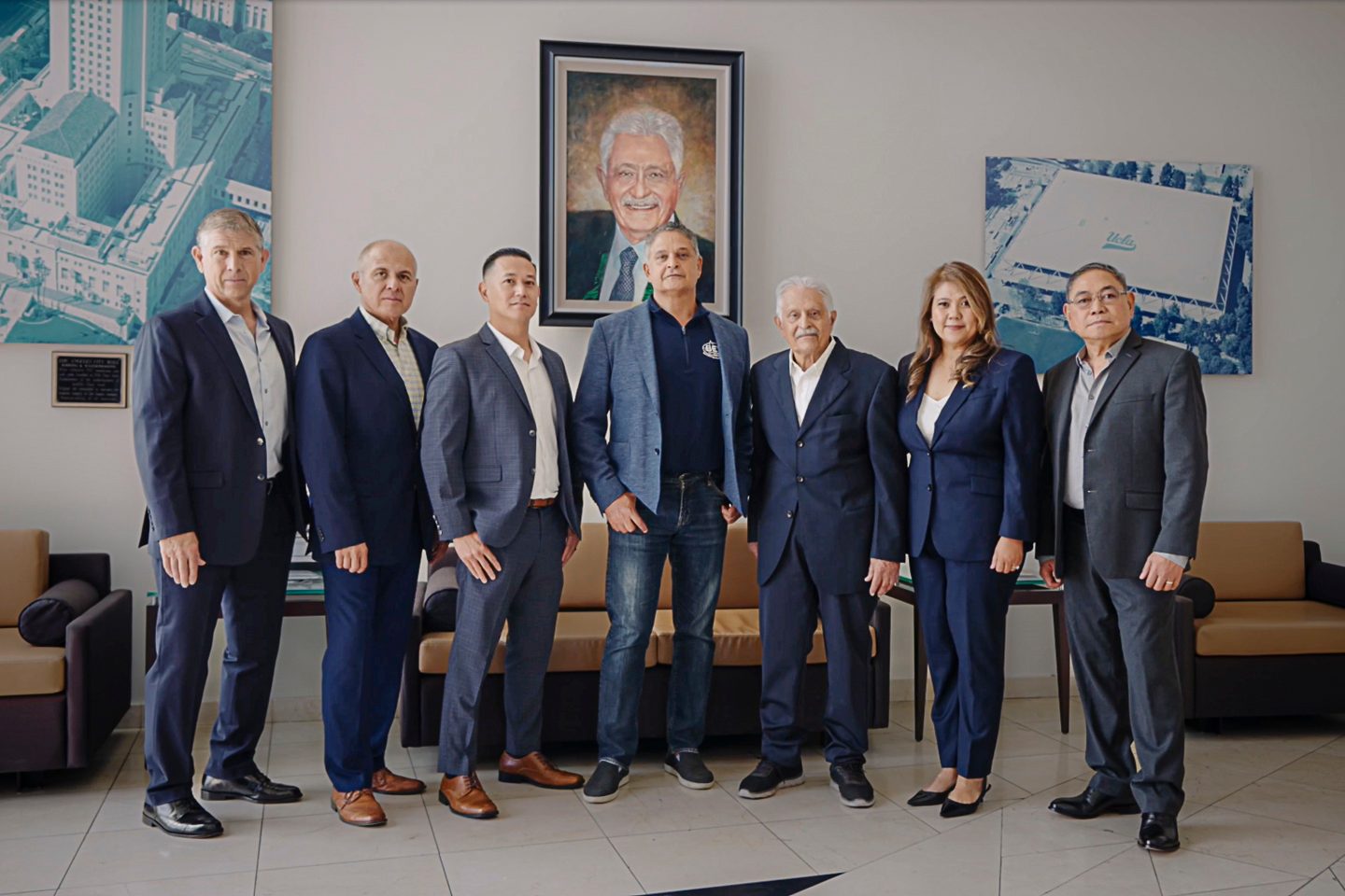 Group photo of seven people, six men and one woman, standing formally indoors with artwork on the wall.