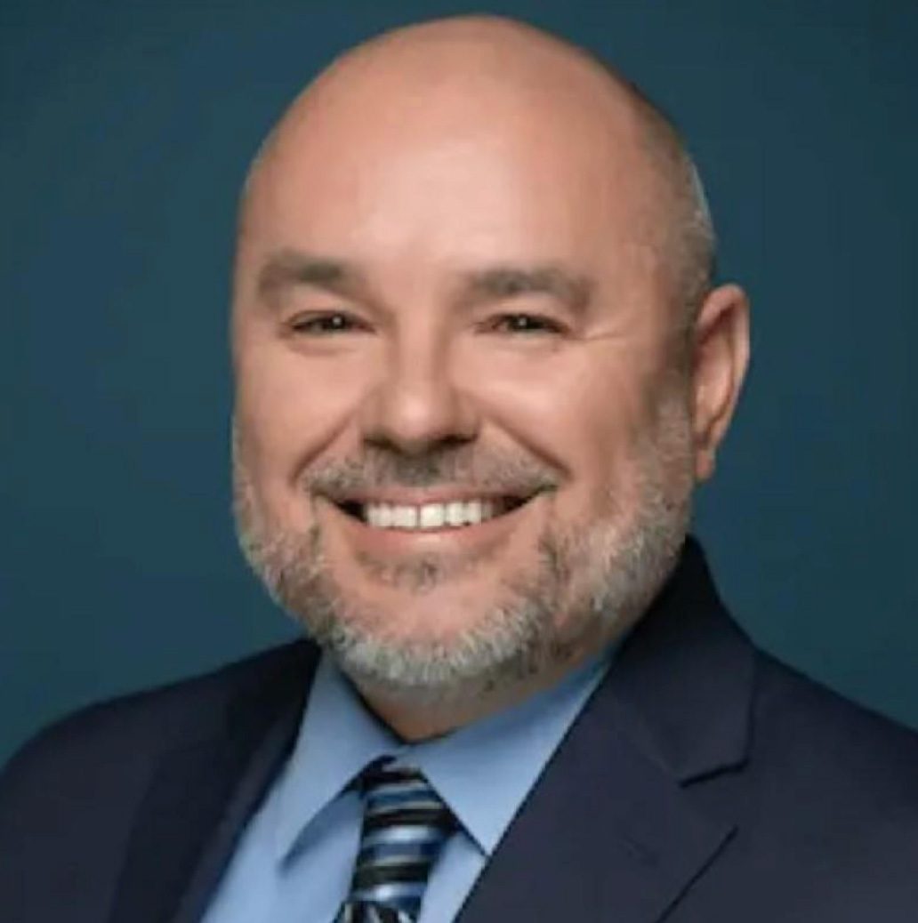 Bald man with a beard and suit smiles warmly at the camera.