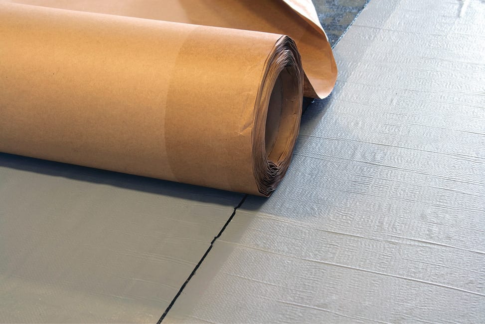 Unrolling brown paper onto a blue textured mat with a dark seam.