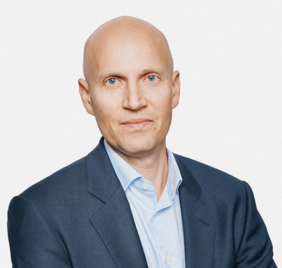Professional headshot of a bald man in a dark blue suit and light blue shirt.