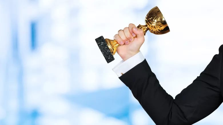Arm in a suit holding a golden trophy aloft against a blurred blue background.