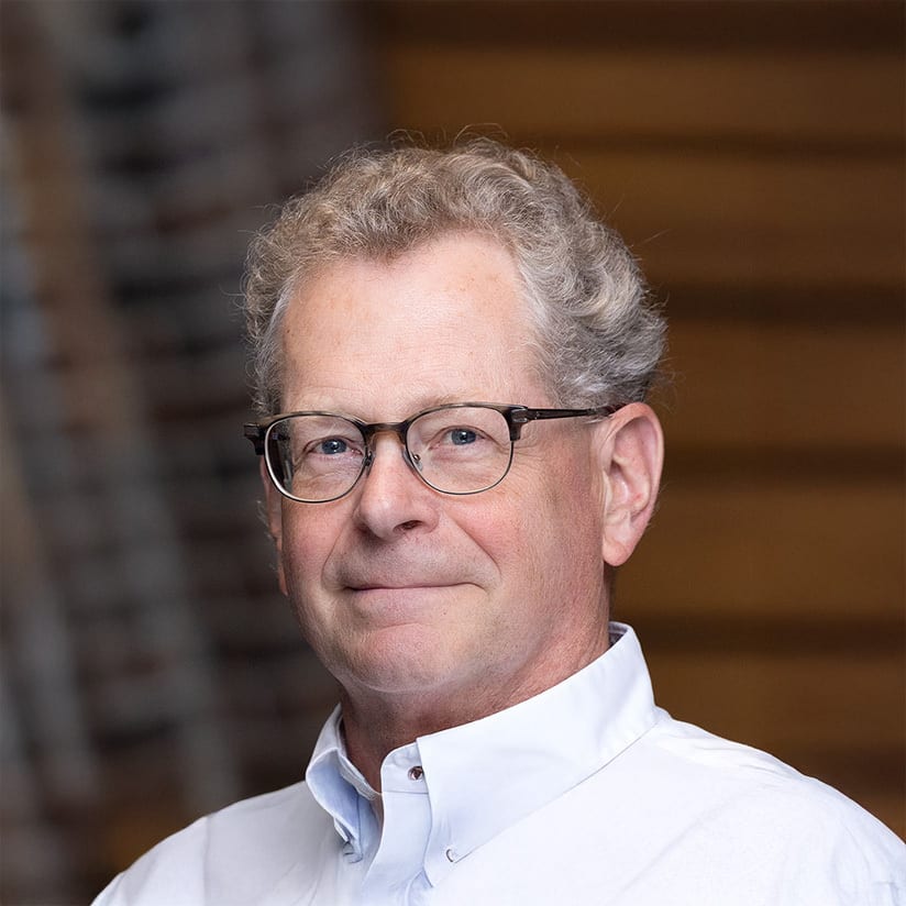 Headshot of a smiling man with glasses, gray curly hair, and a white shirt.