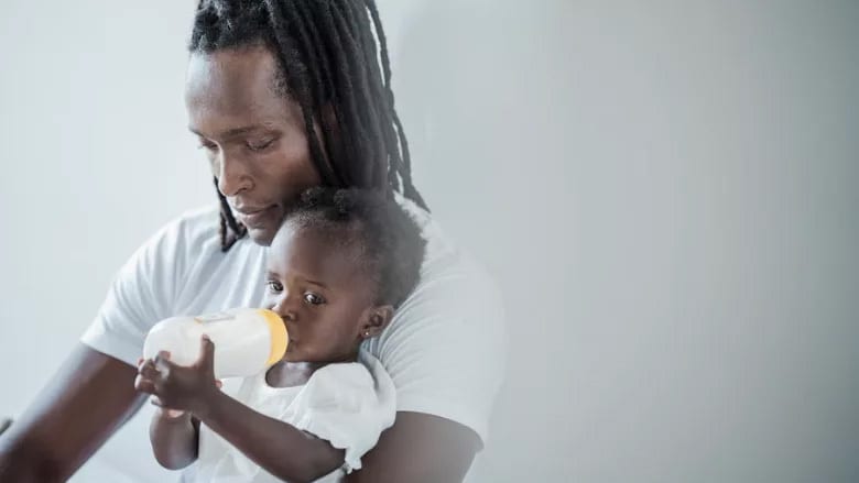 Black father holds baby drinking from bottle.