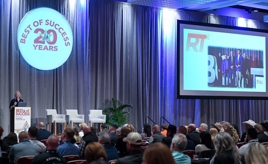 A woman presents to an audience at a conference, with a large "Best of Success 20 Years" sign and screen.