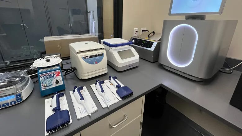 A laboratory bench with various scientific instruments including centrifuges, thermal cyclers, a vortex mixer, and pipettes.