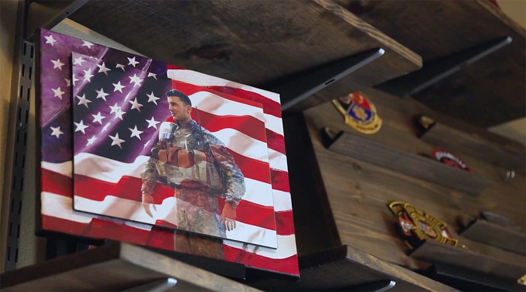 Layered photo of a soldier over an American flag, on wooden shelves with military badges.