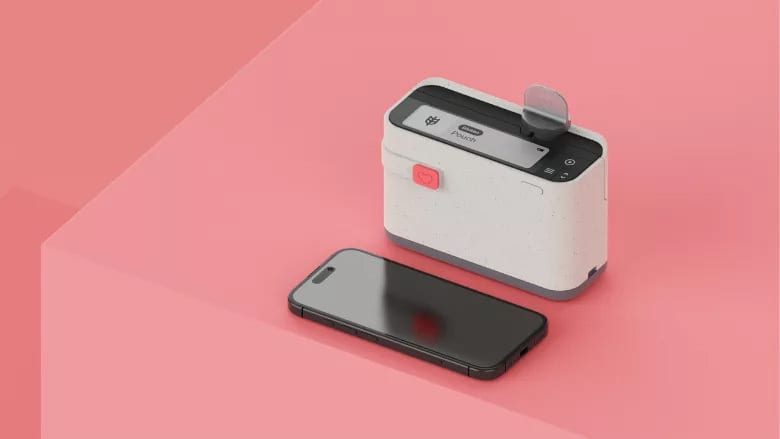 A portable pouch printer with a red heart button and a smartphone on a pink backdrop.