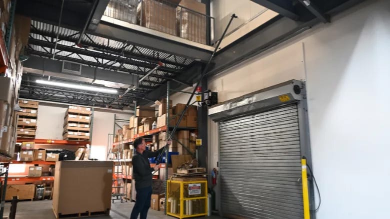 A man operates a roll-up door with a long pole in a warehouse.