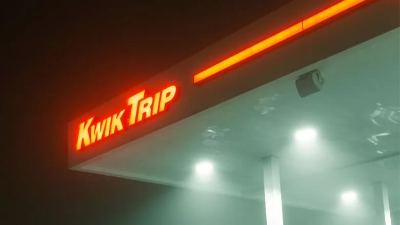 A neon orange 'Kwik Trip' sign illuminates a gas station canopy at night, creating a strong contrast.