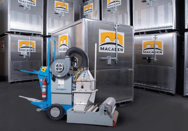 A blue and grey industrial machine for material handling, surrounded by silver Macaden containers.
