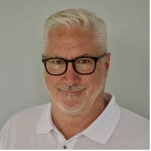 Smiling man with gray hair, glasses, beard, and a white shirt.