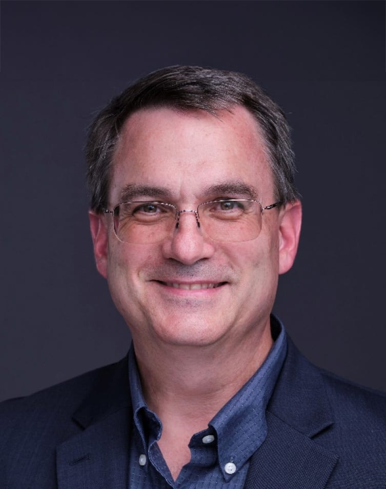 Portrait of a smiling man with glasses, wearing a suit.