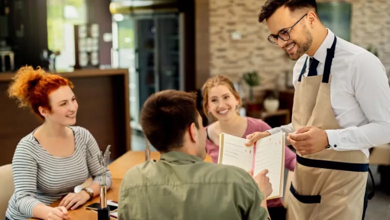 Smiling waiter showing menu to a happy couple in a restaurant.
