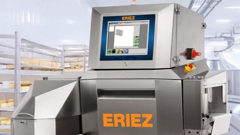 Eriez stainless steel food processing X-ray machine with screen, cheese aging racks behind.