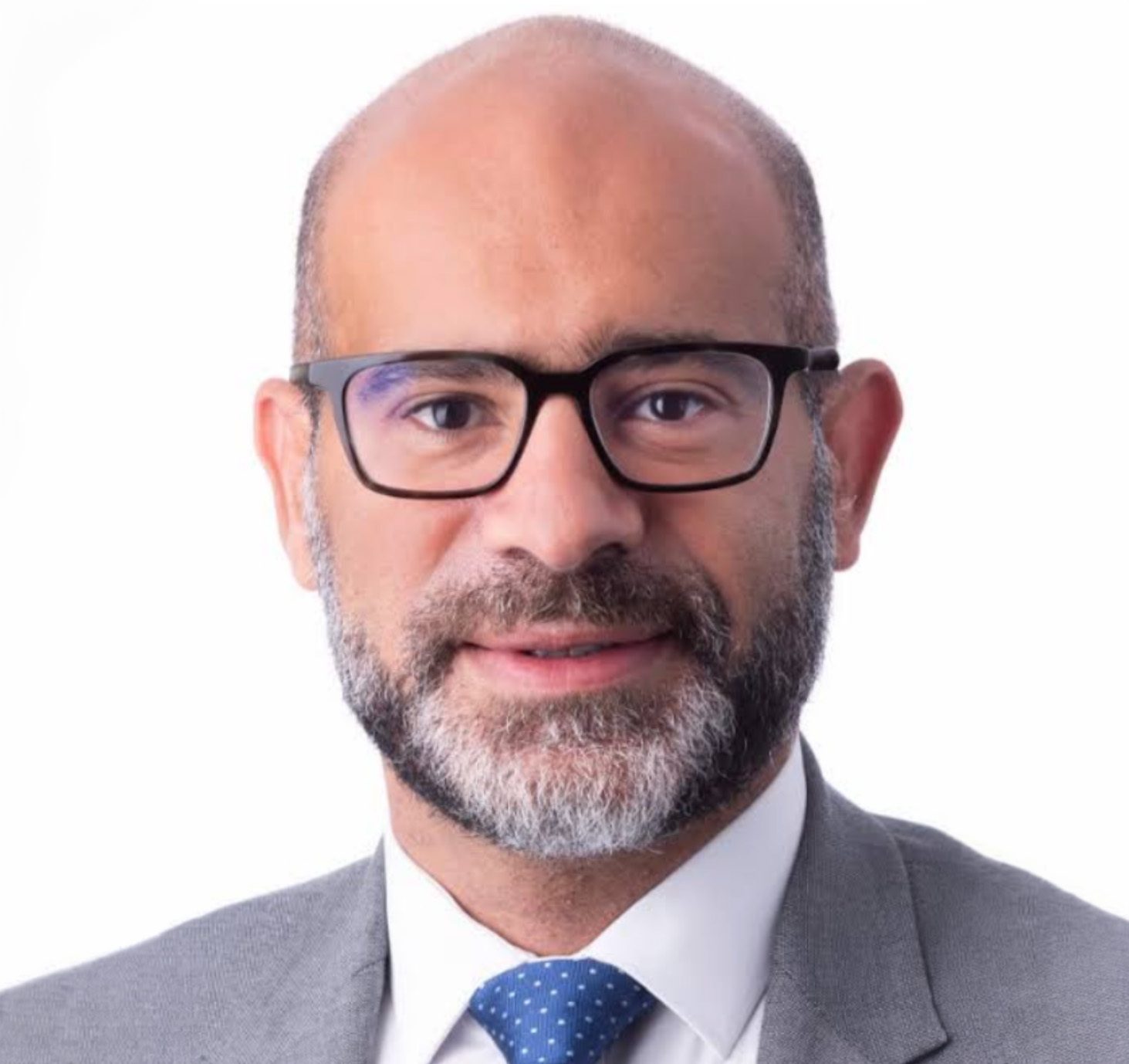 Headshot of a bald man with a beard and glasses, wearing a suit and blue tie, smiling.