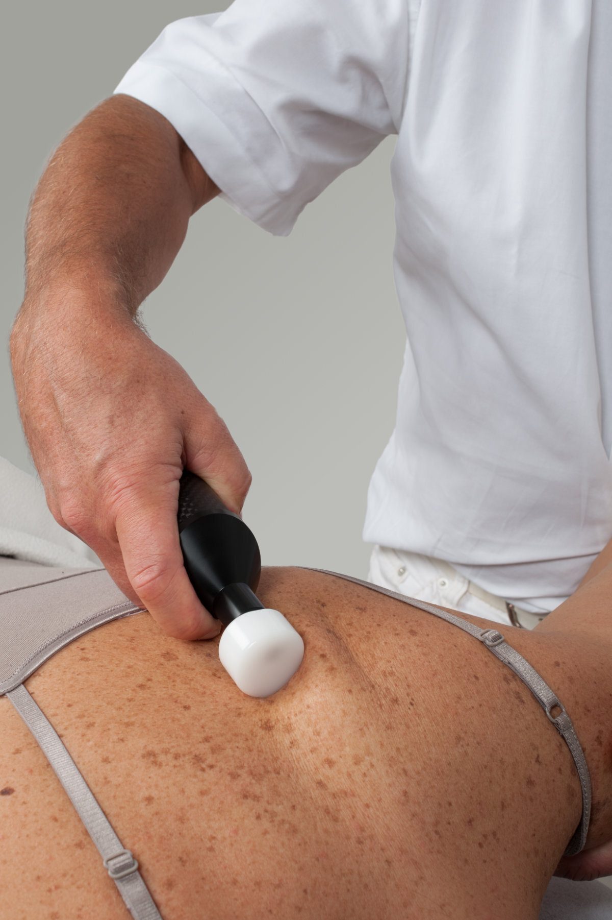 Therapist using medical device on patient's freckled back.