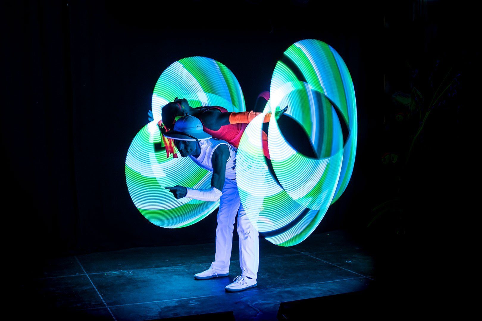 Two performers in dark creating dynamic light trails with glowing hoops, showcasing an artistic and vibrant act.
