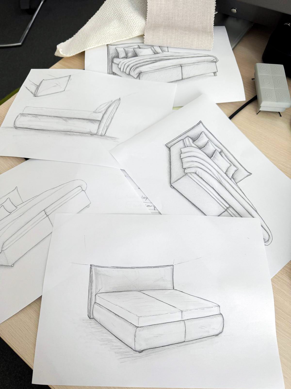 Pencil sketches of various bed designs scattered on a desk, with fabric swatches nearby.