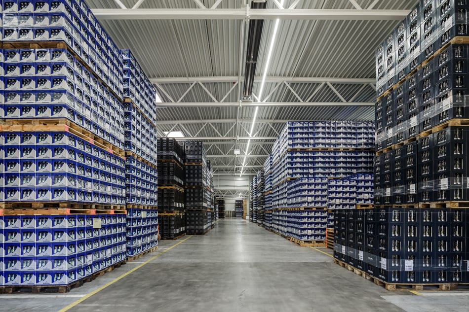 Warehouse interior with towering stacks of boxes and crates on pallets, forming long aisles.