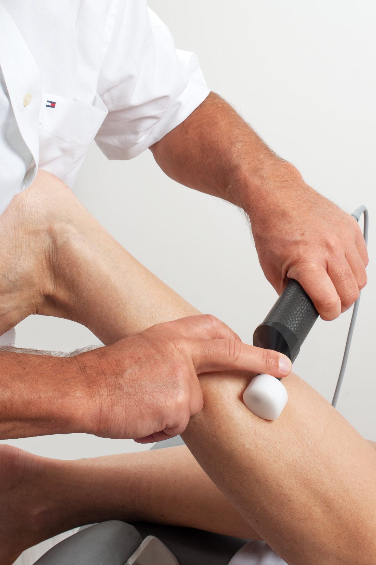 A therapist applies a medical device to a patient's leg, likely for therapy or diagnosis.