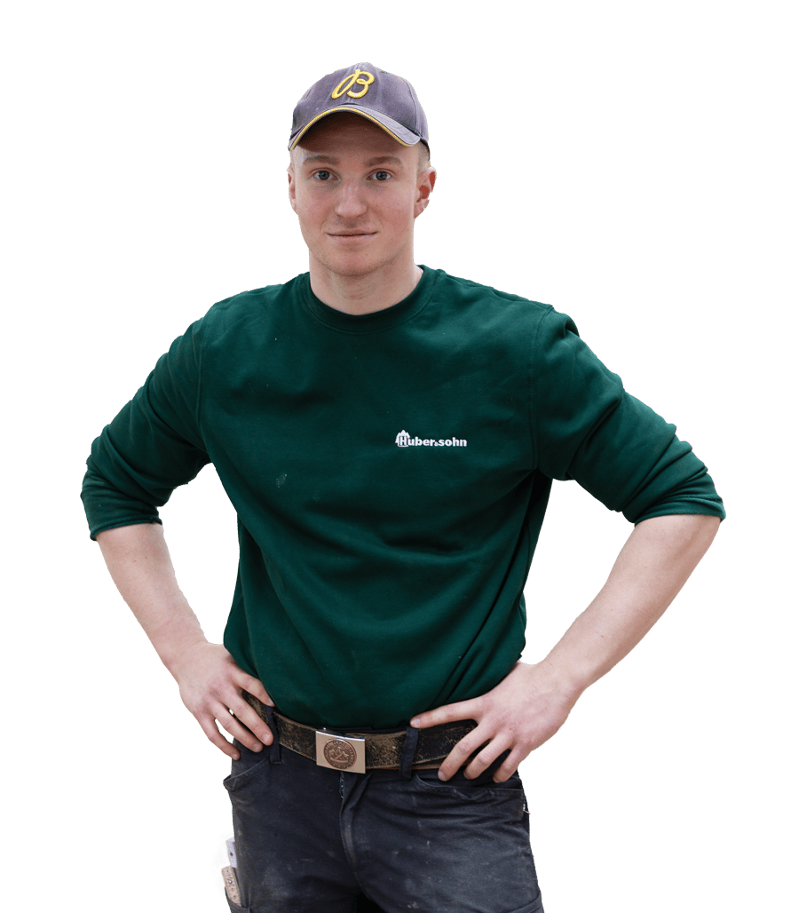 A young man in a green long-sleeve shirt, cap, and dark pants, standing with hands on his hips.