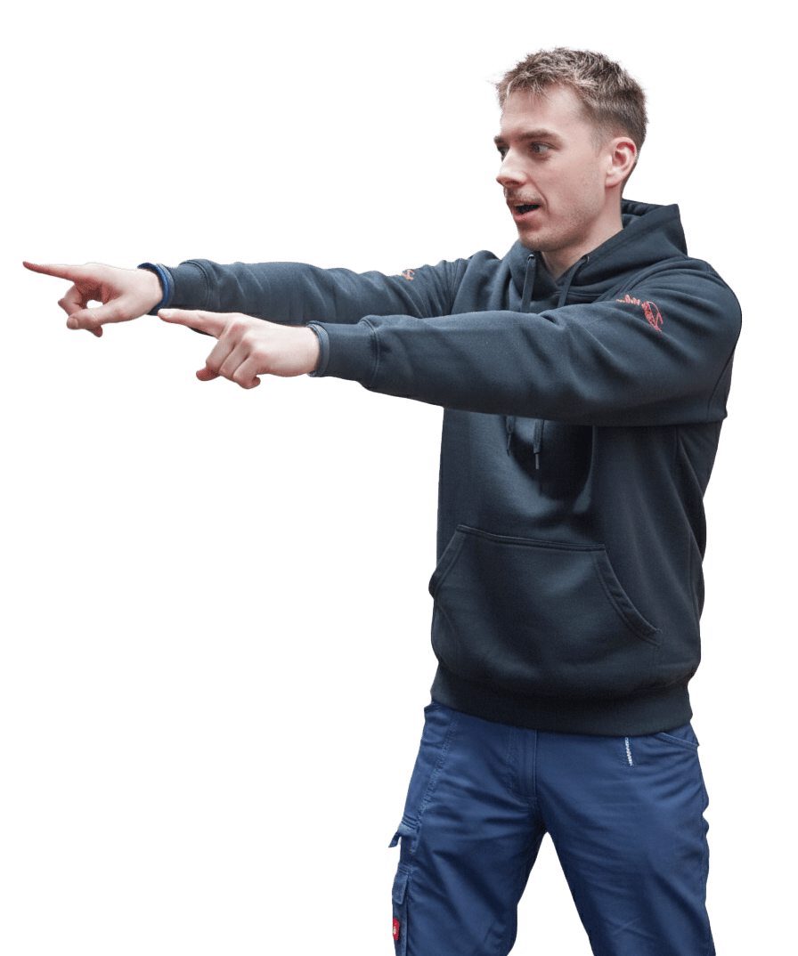 Young man in a dark hoodie and blue pants pointing forward with both hands, mouth slightly open.