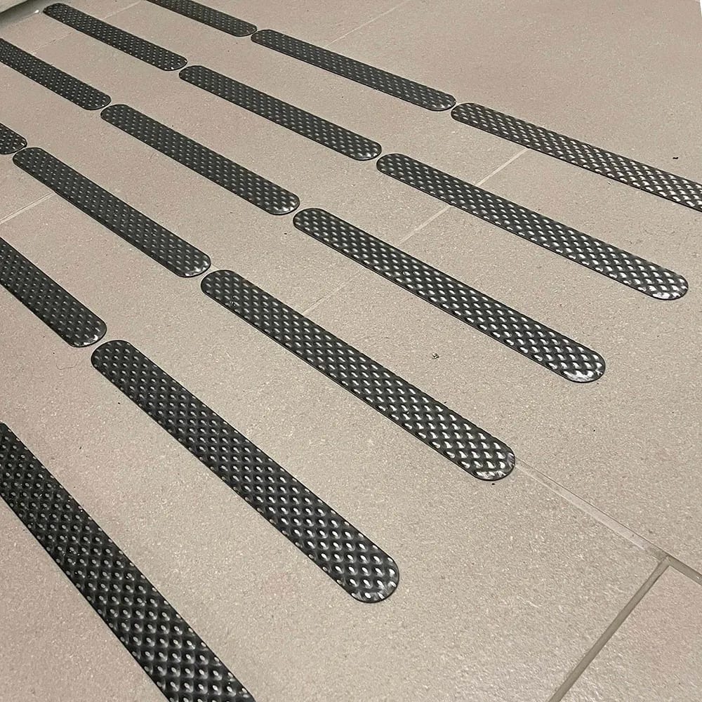 Tactile guidance strips on light tiled floor, arranged in parallel rows.