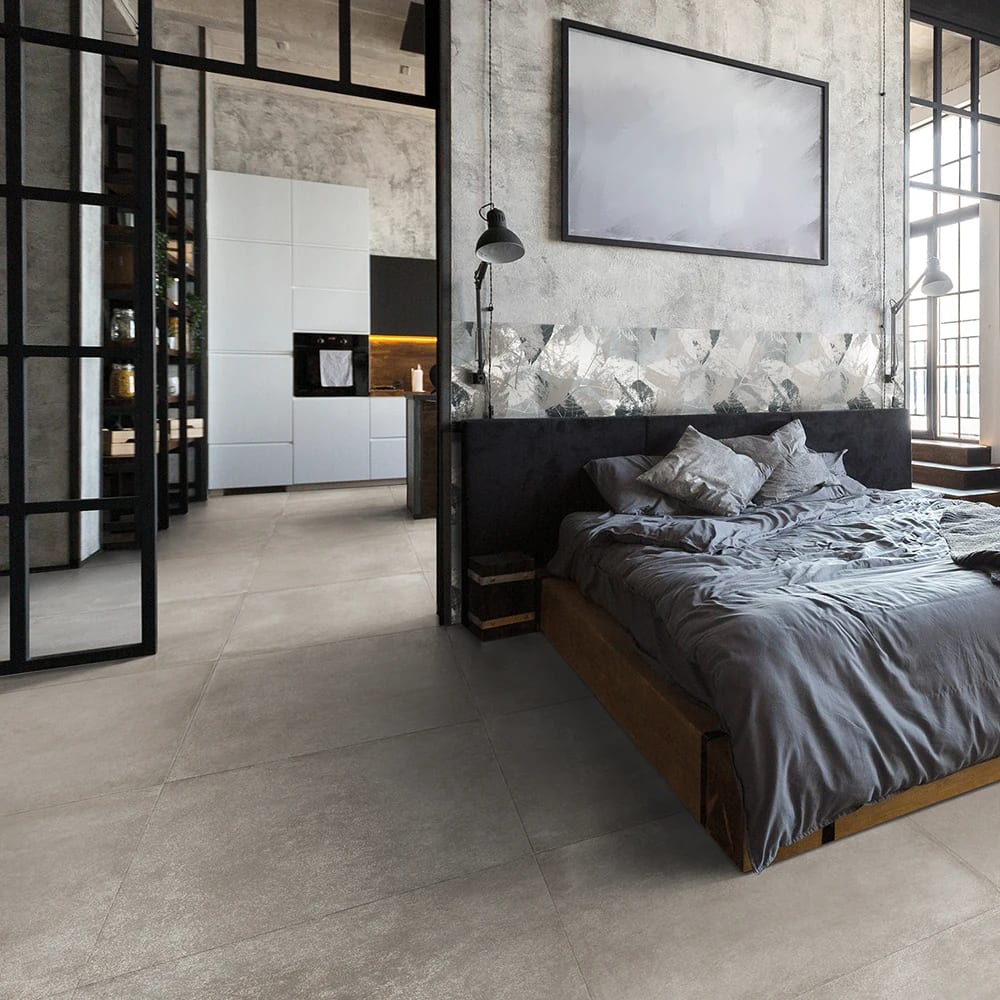 Industrial-style bedroom with grey bed, concrete wall, and view into a modern kitchen.