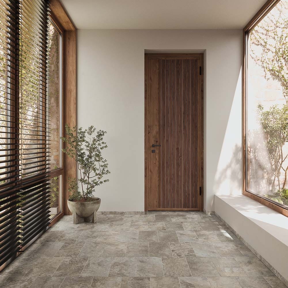 A sunlit hallway featuring a slatted wooden door, a potted plant, and large windows with blinds.