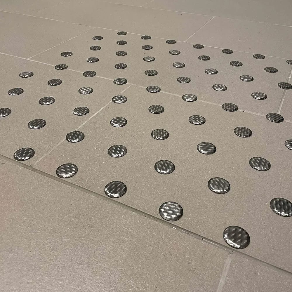 Tactile warning studs embedded in light grey floor tiles.