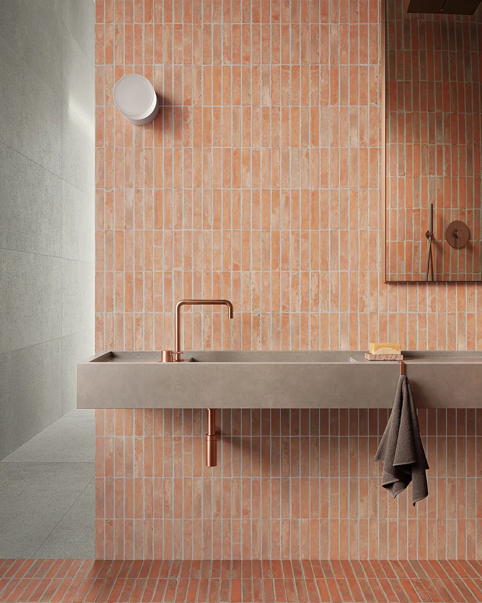 Modern bathroom with terracotta brick tiles, a concrete vanity, and copper fixtures.