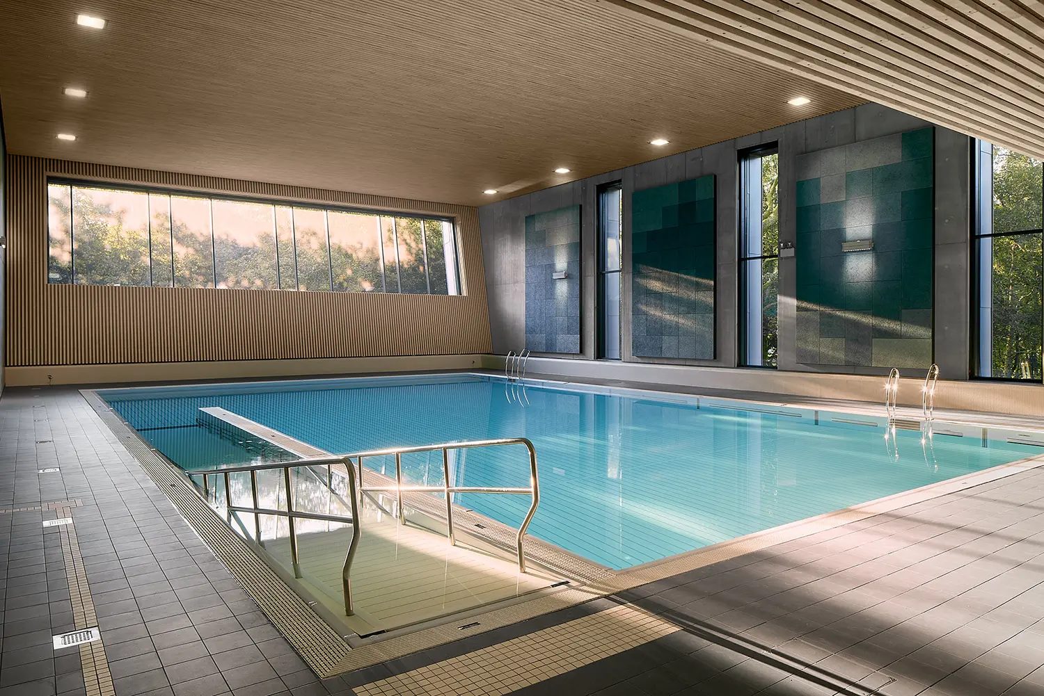 Modern indoor swimming pool featuring large windows, wood accents, and serene blue water.