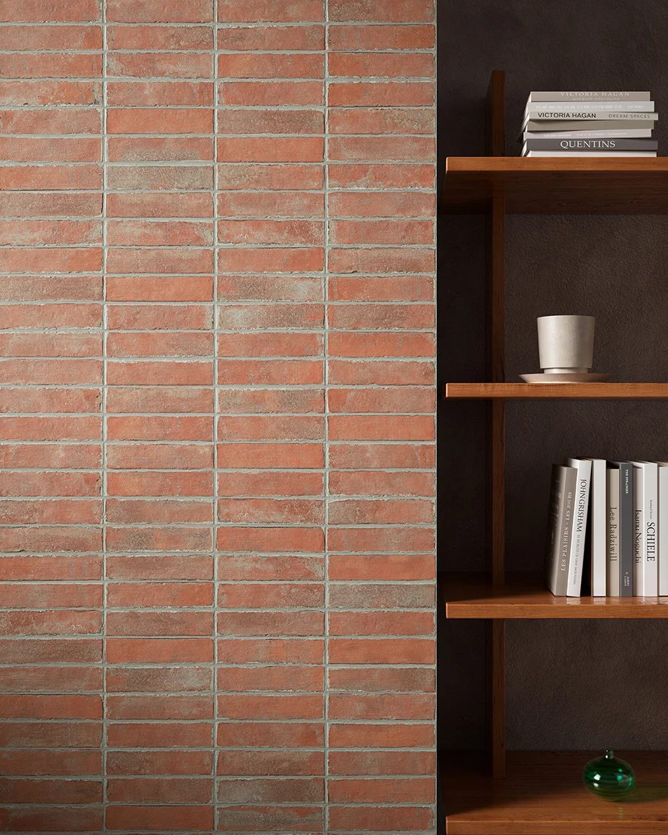 Red brick wall next to a wooden bookshelf with books, a mug, and a green sphere.