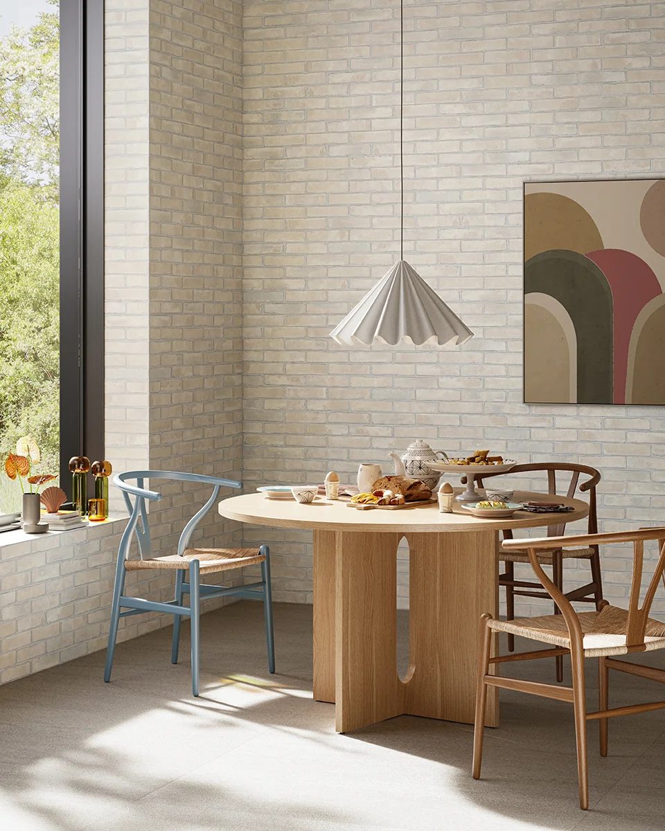 Dining room with round wood table, chairs, breakfast, brick walls, and a pleated pendant light.