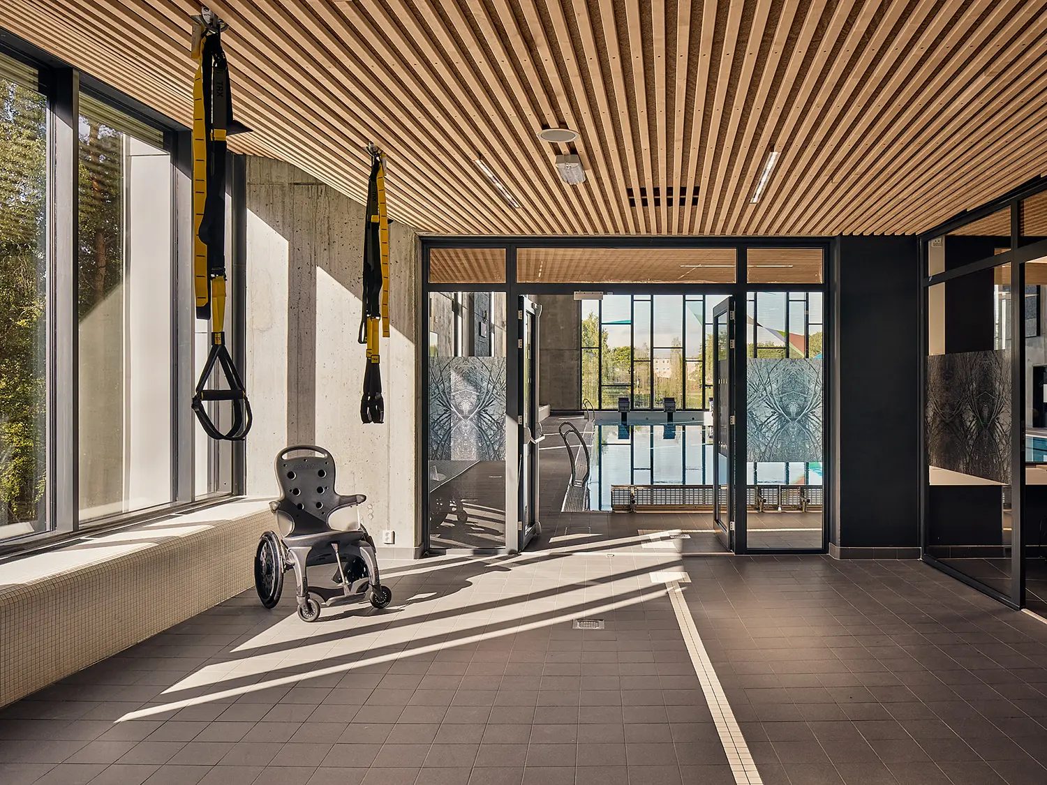 Wheelchair and exercise straps in a bright modern room overlooking a swimming pool.