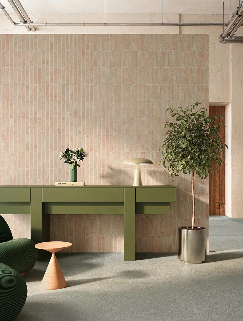 Modern room with pink tiled wall, green console, plant, lamp, and grey floor.